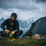 Hiker prepares hot beverage with headlamp in alpine campsite